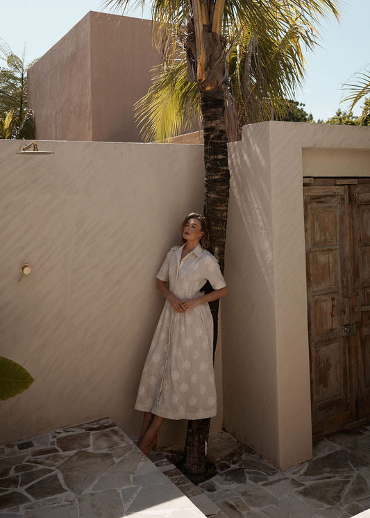 Woman in a white dress standing in a sunlit outdoor setting with palm trees.